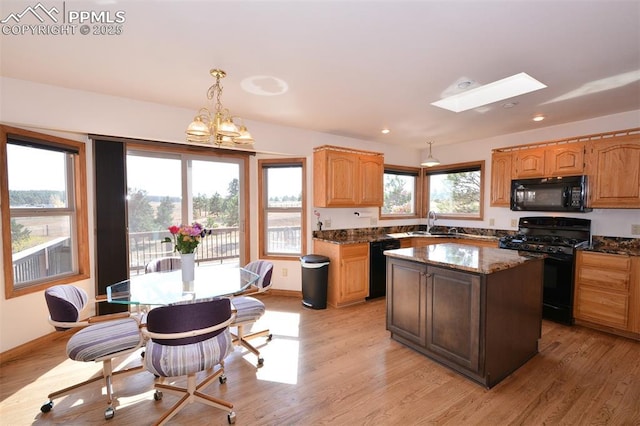 kitchen with a skylight, a sink, a kitchen island, light wood-type flooring, and black appliances