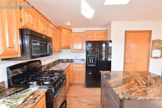 kitchen featuring dark stone counters, black appliances, light wood finished floors, and light brown cabinets