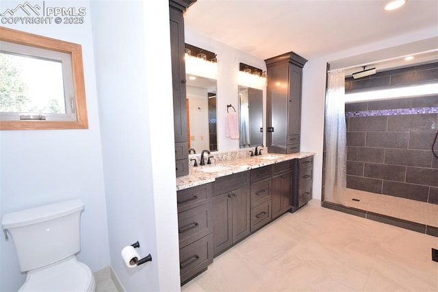 full bath featuring toilet, double vanity, a tile shower, and a sink