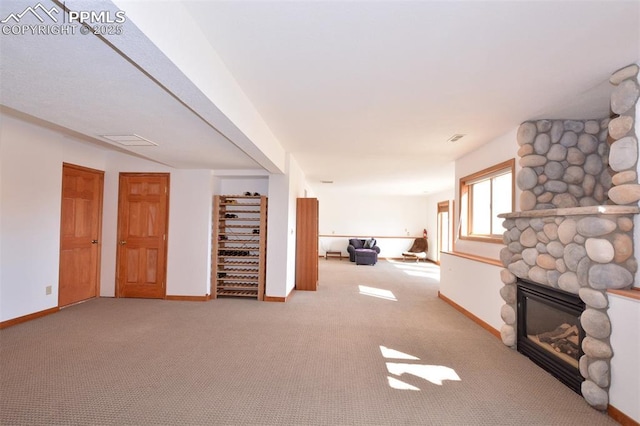 interior space with visible vents, carpet flooring, a stone fireplace, and baseboards