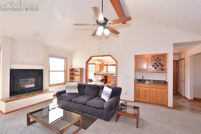 living room with indoor wet bar, light colored carpet, lofted ceiling with beams, a glass covered fireplace, and baseboards