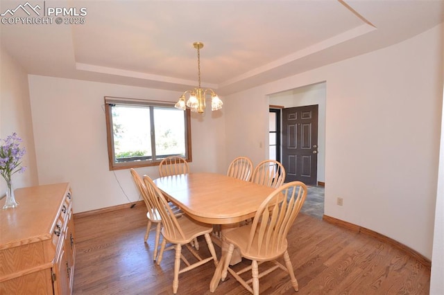 dining space featuring a notable chandelier, baseboards, a tray ceiling, and wood finished floors