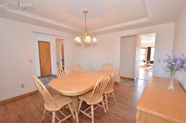 dining space with light wood-style floors, baseboards, a tray ceiling, and an inviting chandelier