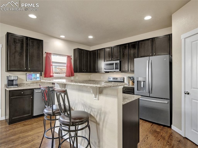 kitchen with stainless steel appliances, a breakfast bar area, recessed lighting, and dark wood-style flooring