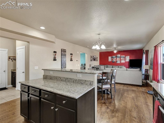 kitchen with open floor plan, a center island, light wood finished floors, decorative light fixtures, and an inviting chandelier