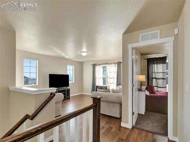 living area with a textured ceiling, dark wood finished floors, visible vents, and baseboards