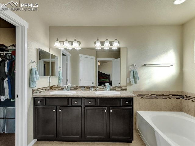 bathroom with a garden tub, double vanity, a sink, and a walk in closet