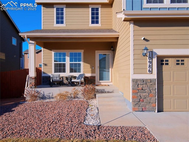 view of exterior entry with a garage, stone siding, a porch, and fence