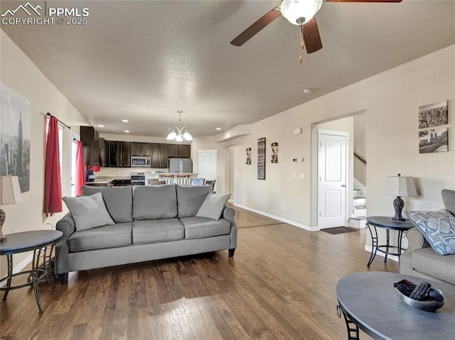 living area with ceiling fan with notable chandelier, stairway, dark wood finished floors, and baseboards