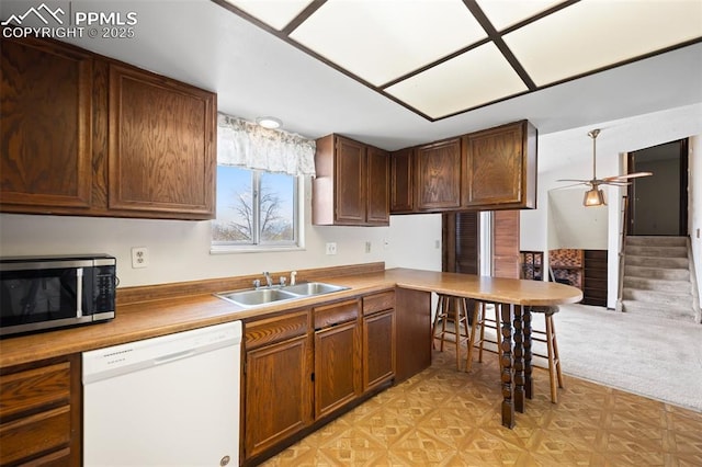 kitchen featuring ceiling fan, dishwasher, a sink, stainless steel microwave, and a peninsula