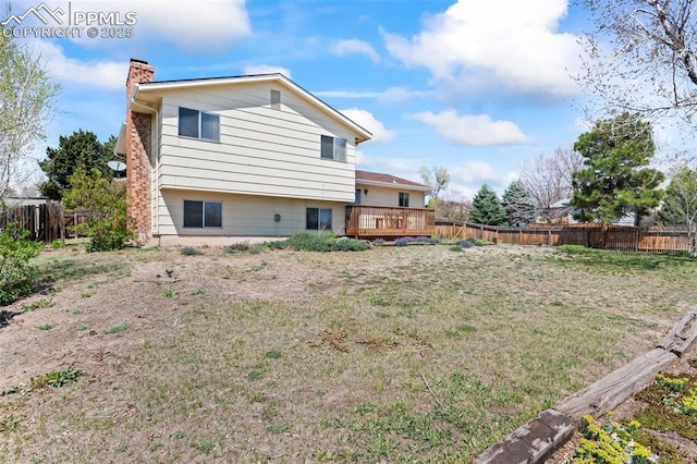 back of property with a fenced backyard, a chimney, a lawn, and a deck