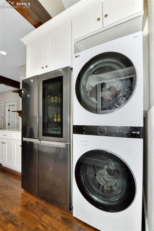 washroom with dark wood-style flooring, stacked washing maching and dryer, and laundry area