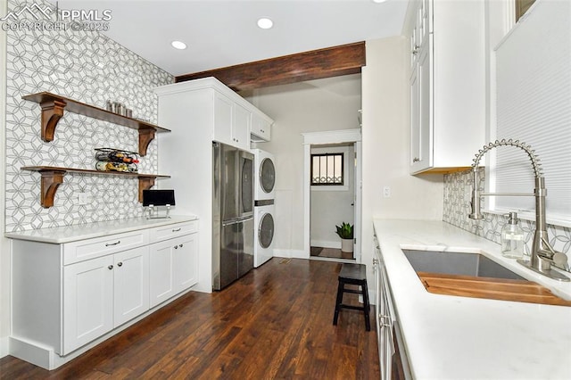 kitchen featuring stacked washer and dryer, a sink, white cabinetry, freestanding refrigerator, and dark wood-style floors