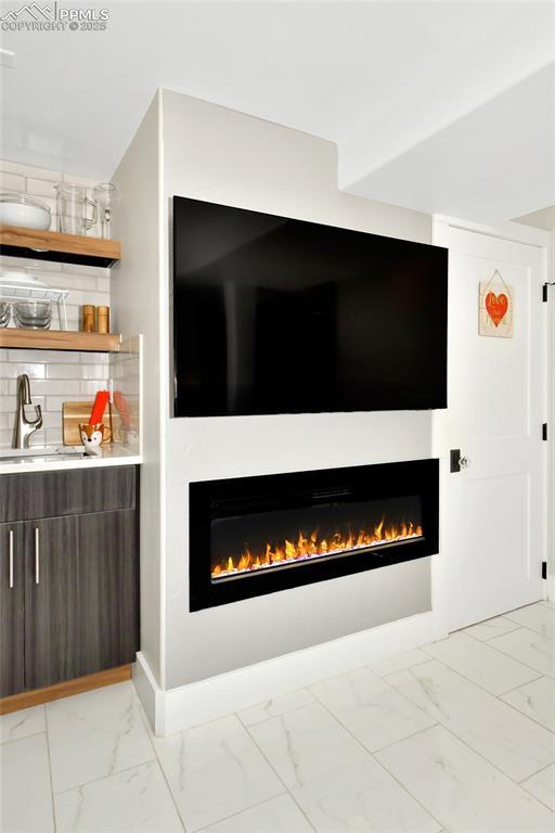 interior details with a sink, a warm lit fireplace, baseboards, and backsplash