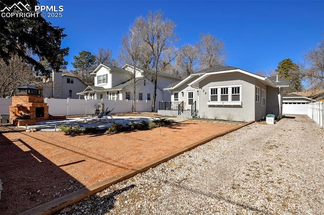 rear view of house with stucco siding, a patio area, a stone fireplace, and a fenced backyard