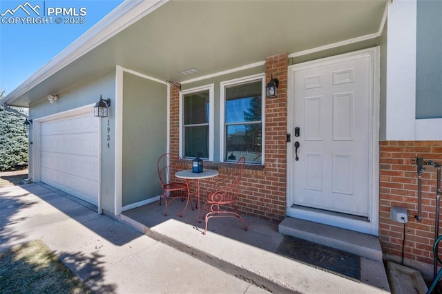 entrance to property with a garage, brick siding, and covered porch