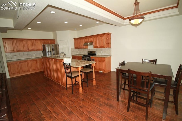 kitchen featuring stainless steel appliances, dark wood-type flooring, a center island with sink, and under cabinet range hood