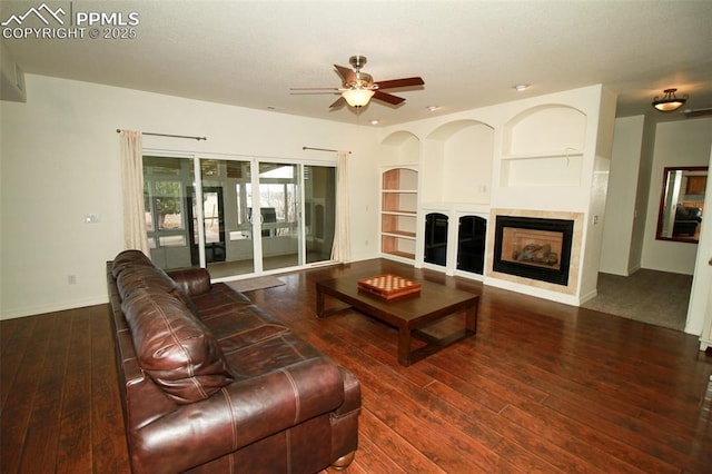 living area featuring baseboards, built in features, a ceiling fan, hardwood / wood-style floors, and a fireplace