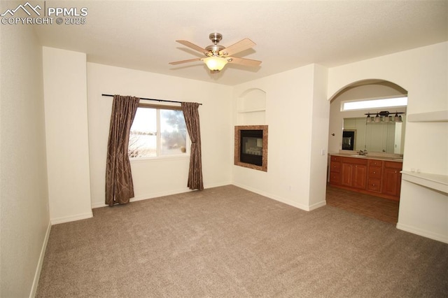 unfurnished living room with carpet floors, a glass covered fireplace, a sink, and a ceiling fan