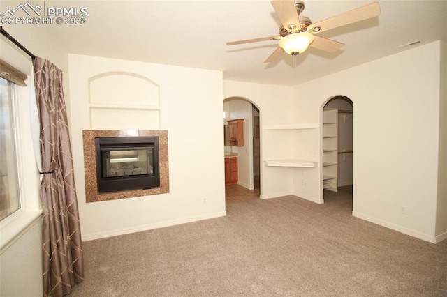 unfurnished living room with arched walkways, carpet flooring, visible vents, and baseboards