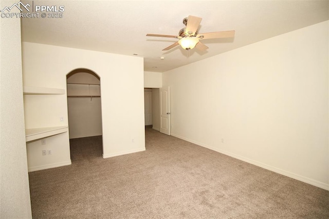 unfurnished bedroom featuring ceiling fan, carpet floors, baseboards, a closet, and a walk in closet