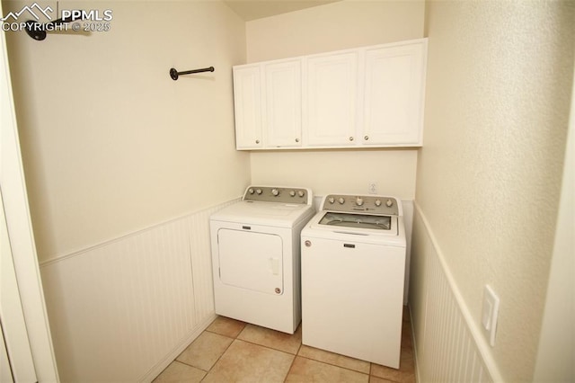 washroom featuring a wainscoted wall, light tile patterned flooring, washing machine and clothes dryer, and cabinet space