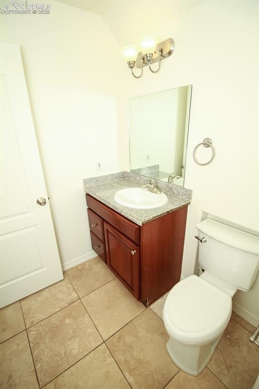 bathroom featuring tile patterned flooring, toilet, vanity, baseboards, and vaulted ceiling