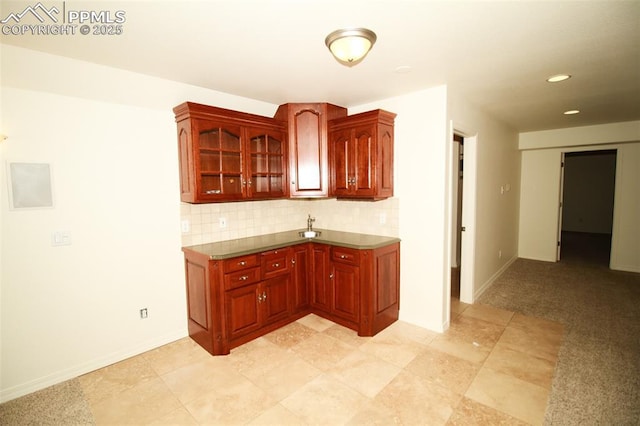 kitchen with reddish brown cabinets, tasteful backsplash, glass insert cabinets, light carpet, and baseboards