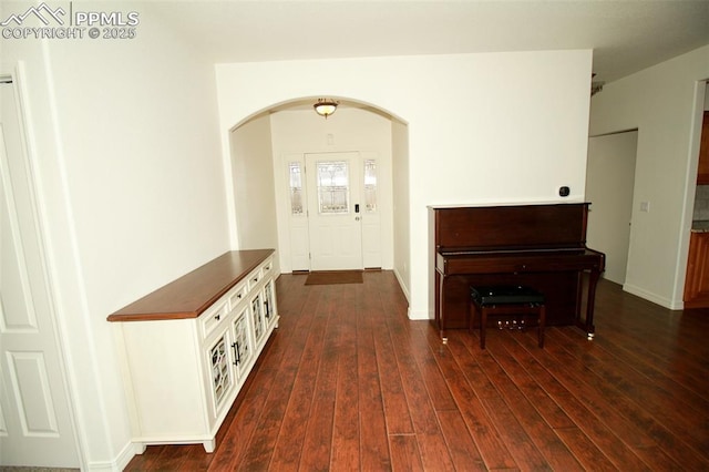 foyer featuring dark wood-style floors, arched walkways, and baseboards