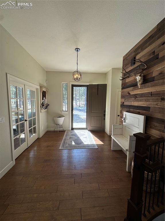 entrance foyer featuring dark wood-style floors, french doors, a chandelier, and wood walls