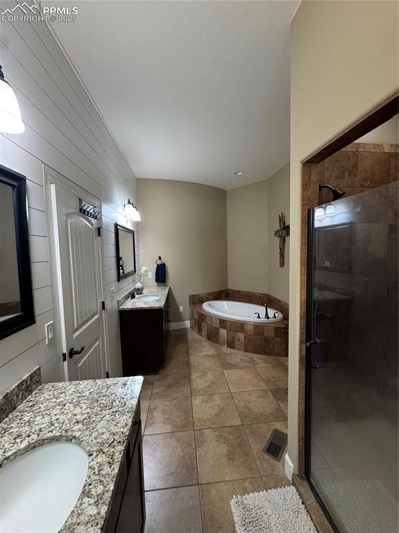 bathroom with tile patterned flooring, a sink, two vanities, a bath, and a stall shower