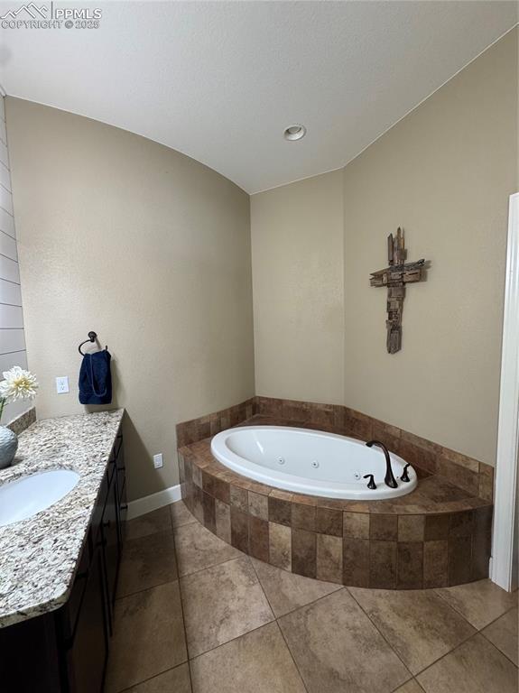 full bath with a whirlpool tub, tile patterned flooring, vanity, and baseboards