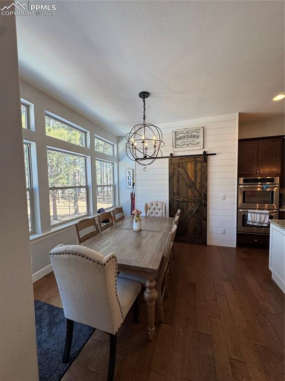 dining space with an inviting chandelier, a barn door, dark wood finished floors, and a textured ceiling