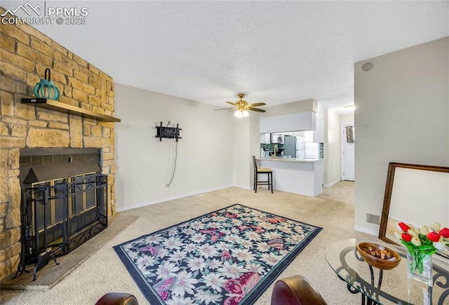 living area with visible vents, light colored carpet, ceiling fan, a stone fireplace, and a textured ceiling