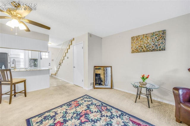 interior space with light carpet, baseboards, ceiling fan, stairs, and a fireplace