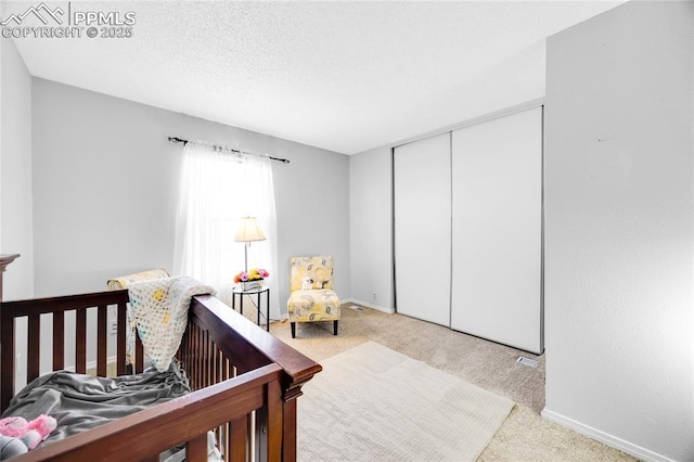 bedroom with a crib, baseboards, a textured ceiling, and light colored carpet