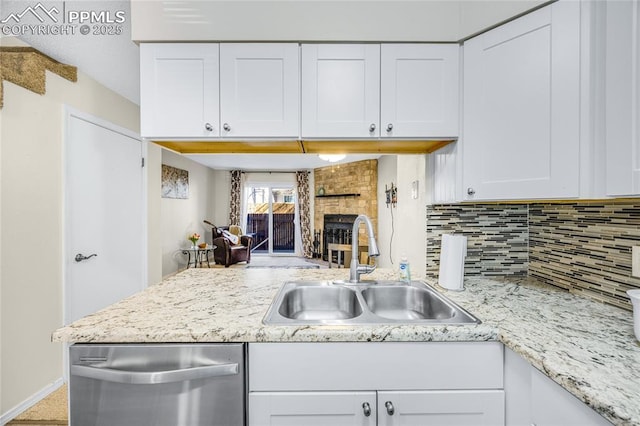 kitchen with a fireplace, a sink, white cabinets, stainless steel dishwasher, and backsplash