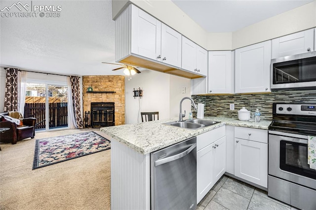 kitchen featuring tasteful backsplash, appliances with stainless steel finishes, open floor plan, a fireplace, and a sink