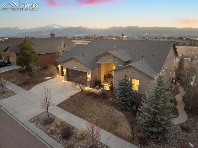 view of front of house featuring roof with shingles, a mountain view, a garage, stone siding, and driveway