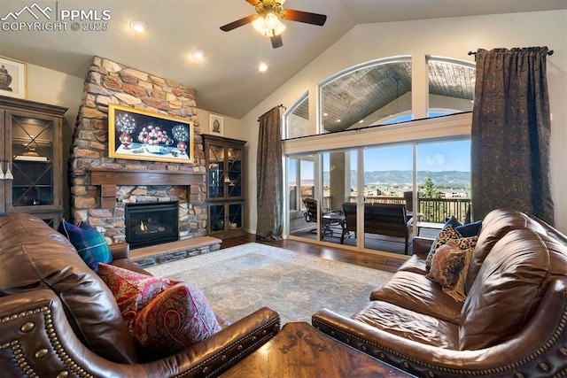 living area featuring lofted ceiling, ceiling fan, a mountain view, a stone fireplace, and wood finished floors