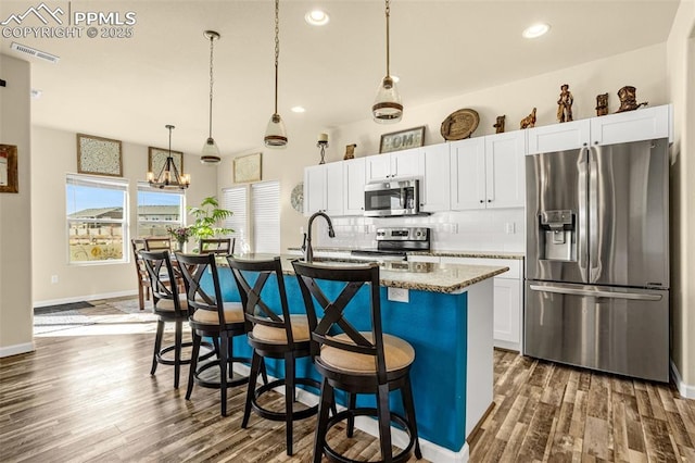 kitchen with dark wood finished floors, visible vents, backsplash, appliances with stainless steel finishes, and a kitchen island with sink