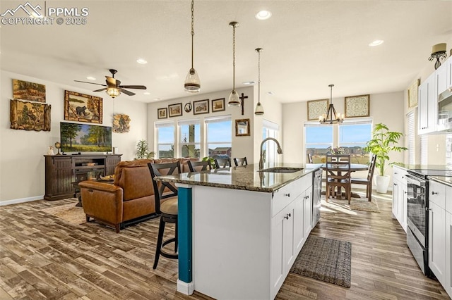 kitchen with a kitchen island with sink, dark wood-type flooring, a sink, and stainless steel range with electric stovetop