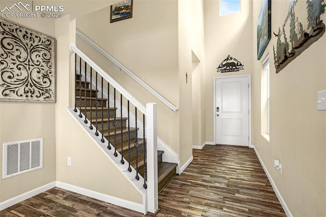 entryway with a towering ceiling, dark wood finished floors, visible vents, and baseboards