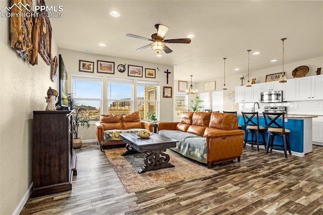 living area with ceiling fan with notable chandelier, dark wood-style flooring, baseboards, and recessed lighting