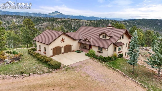 view of front of property featuring dirt driveway, a forest view, a mountain view, and stucco siding