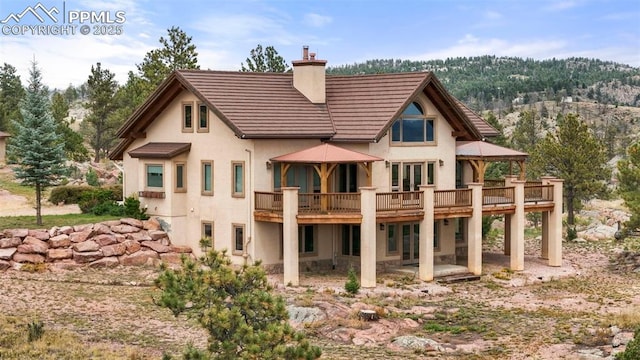 rear view of property with a patio, french doors, a wooden deck, stucco siding, and a chimney