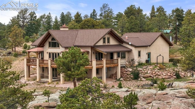 rear view of house featuring a chimney, stucco siding, a patio area, a tiled roof, and a wooden deck