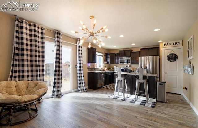 kitchen with appliances with stainless steel finishes, a notable chandelier, a center island, light wood-style flooring, and dark brown cabinets