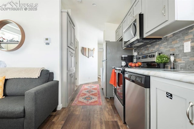 kitchen with dark wood-style flooring, light countertops, decorative backsplash, appliances with stainless steel finishes, and baseboards