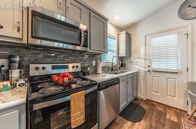 kitchen featuring gray cabinetry, stainless steel appliances, a sink, light countertops, and tasteful backsplash